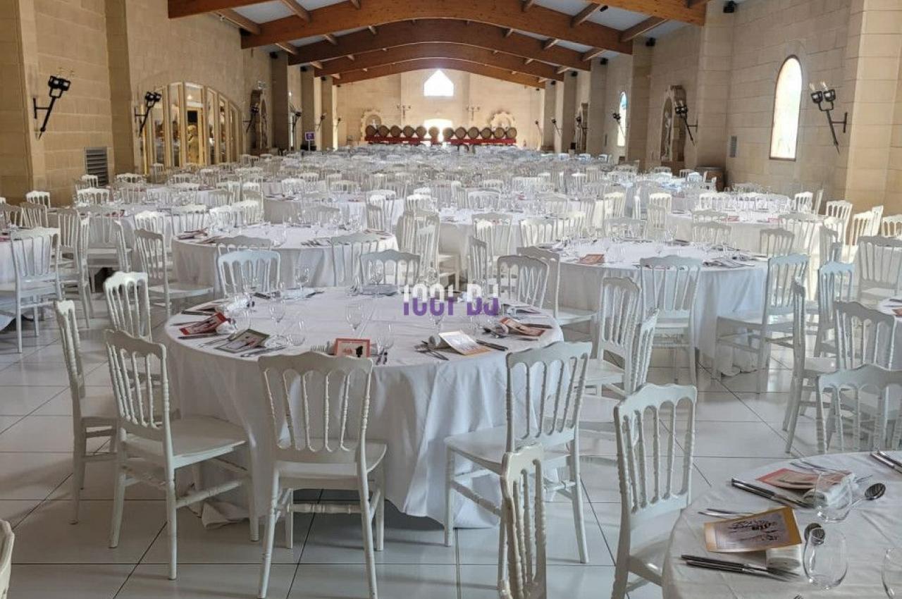 Salle de réception spacieuse avec des tables rondes dressées, nappes blanches et chaises alignées.