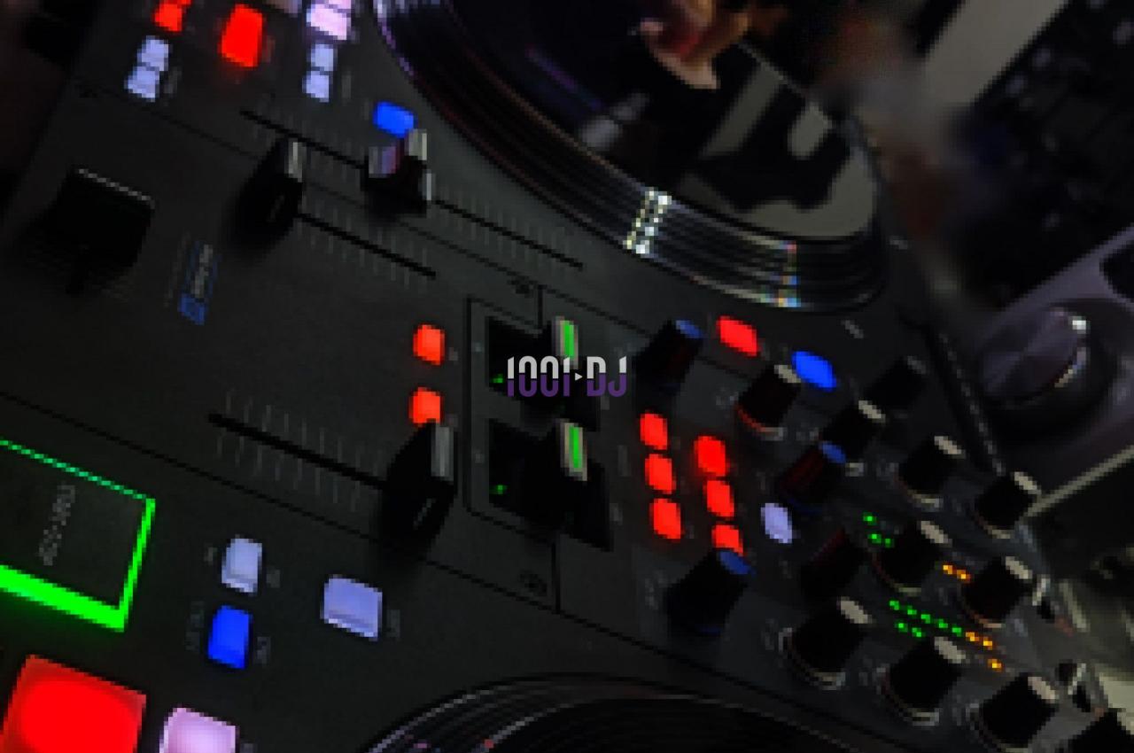 Table de mixage avec platines et boutons lumineux, accompagnée d'écrans affichant des interfaces de mixage audio.
