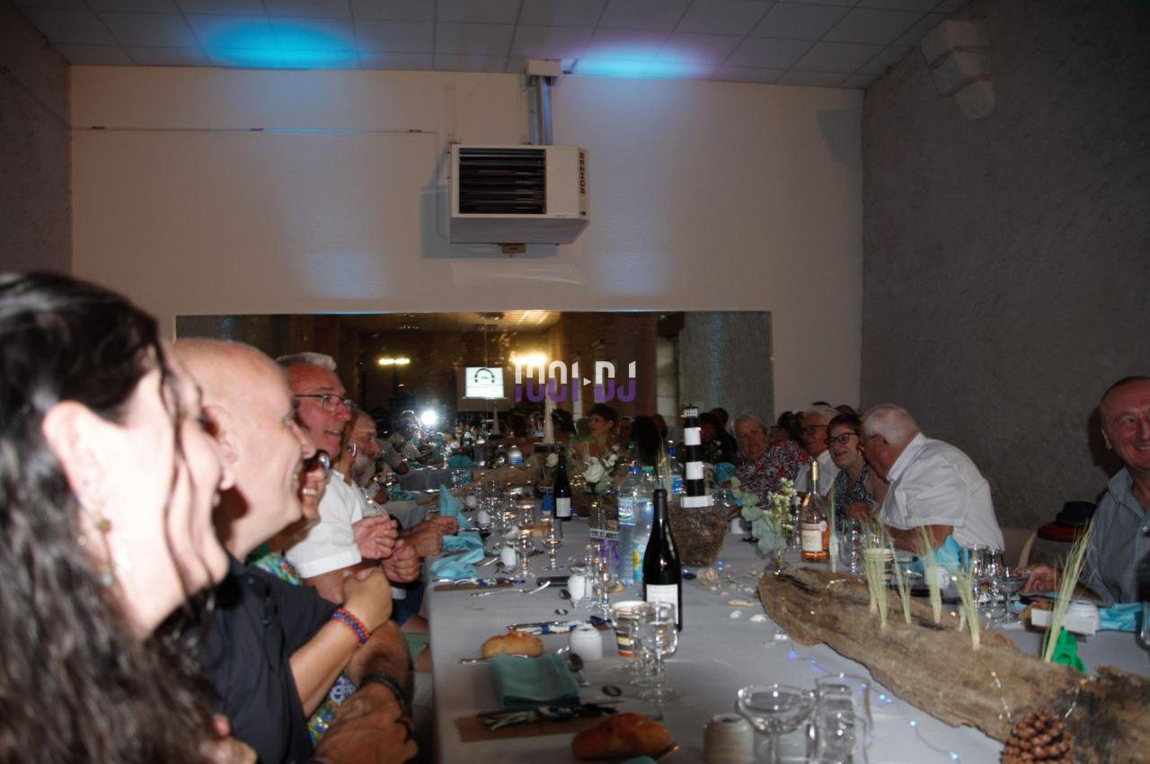 Des convives assis autour d'une longue table décorée, partageant un repas dans une salle éclairée.