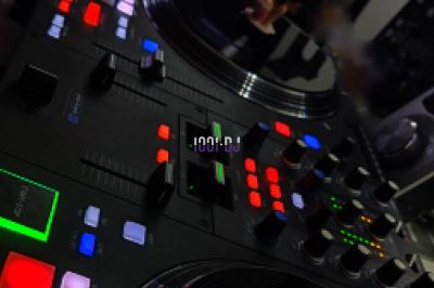 Table de mixage avec platines et boutons lumineux, accompagnée d'écrans affichant des interfaces de mixage audio.