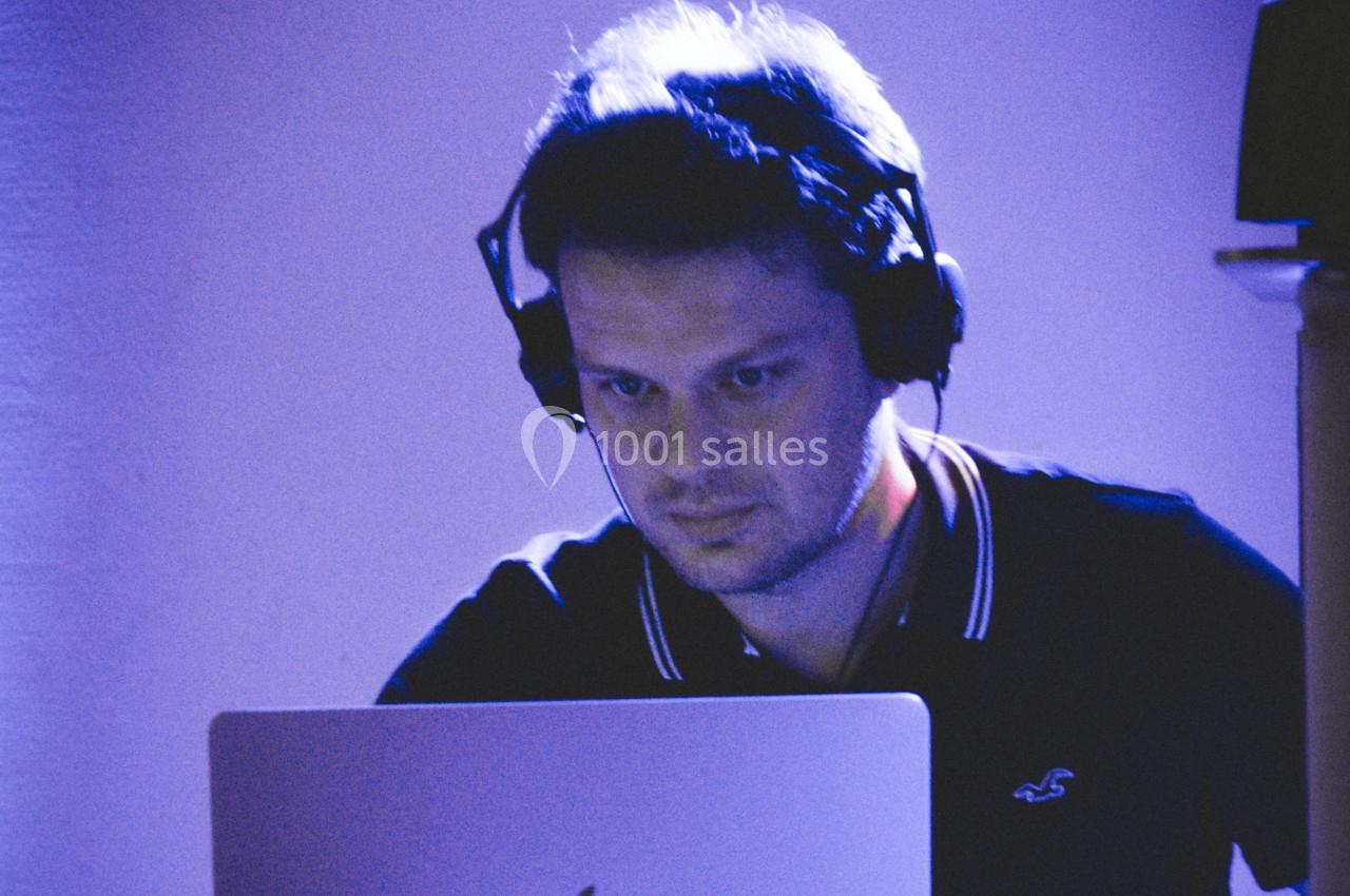 Homme portant un casque audio, concentré devant un ordinateur portable dans un environnement éclairé en bleu.