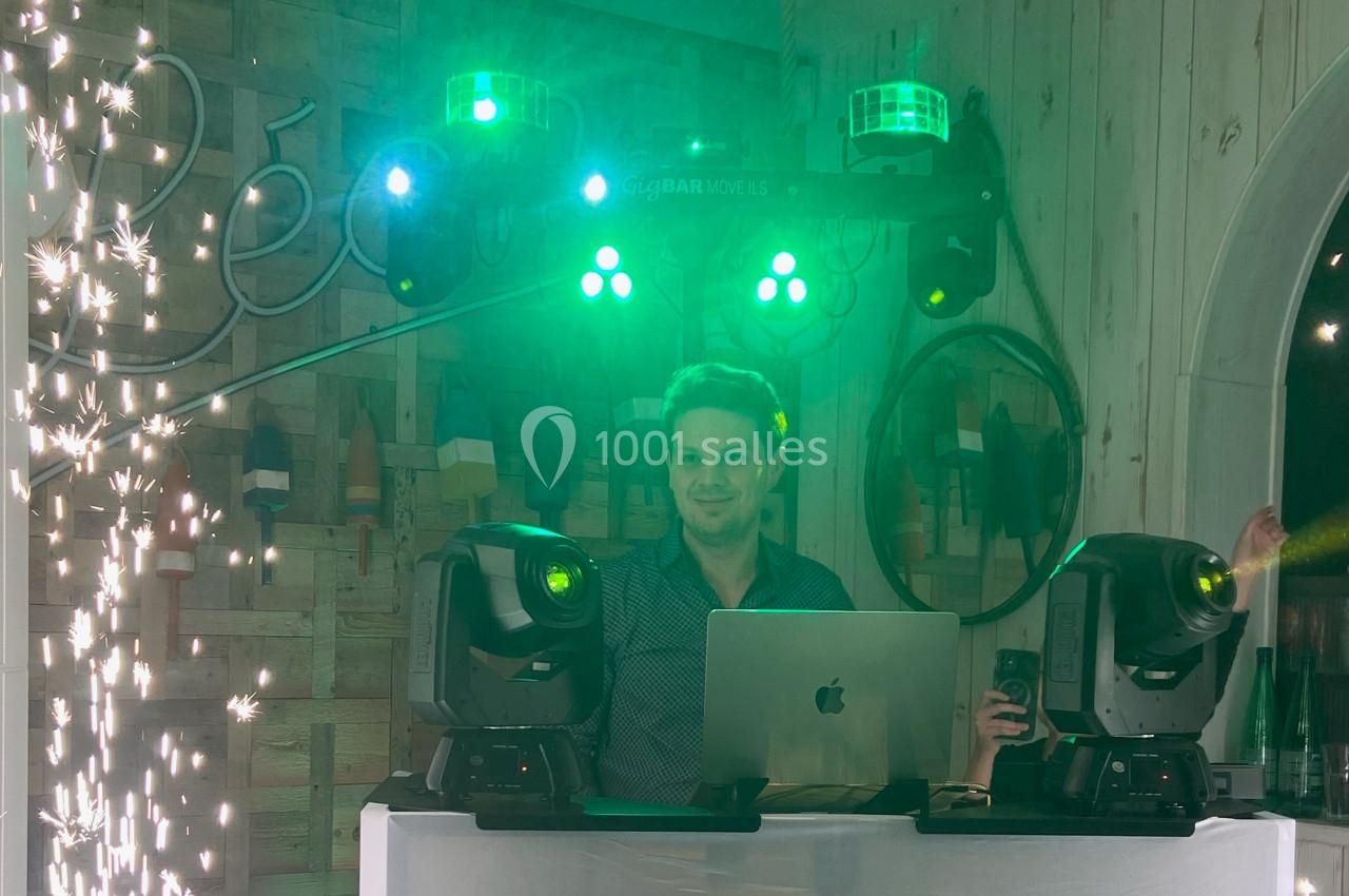 Un DJ mixe derrière un ordinateur portable, entouré de jeux de lumière verts et d'effets pyrotechniques.