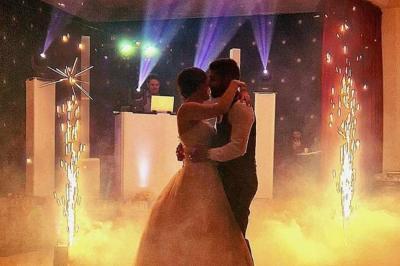 Un couple danse dans une ambiance festive avec éclairages colorés, fumée et étincelles décoratives.