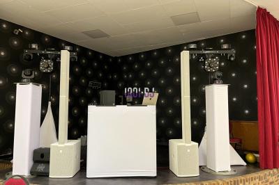 Un DJ mixe sur un ordinateur portable, entouré de lumières colorées dans un décor en bois avec des bouées suspendues.