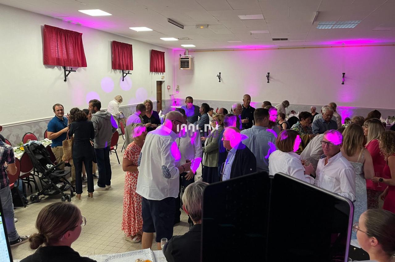 Des personnes discutent et dansent dans une salle éclairée par des lumières roses, lors d'un événement festif.