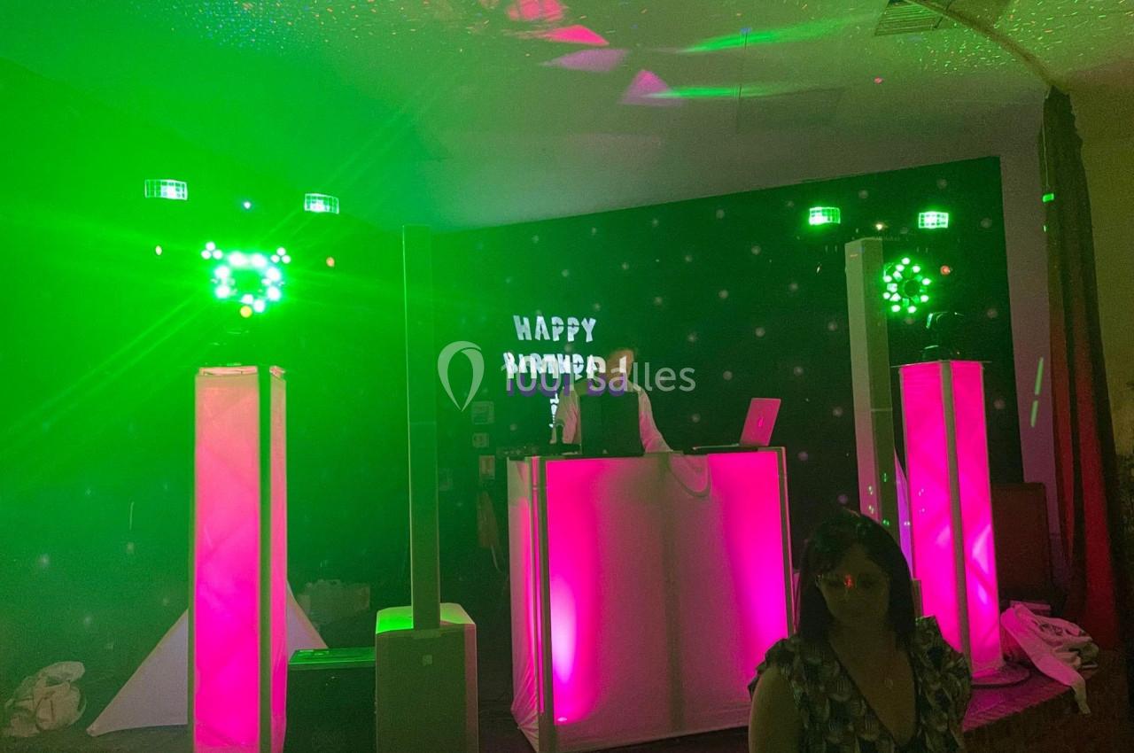 Un DJ anime une soirée avec des lumières vertes et roses sur une scène décorée d'un panneau ’Happy Birthday’.