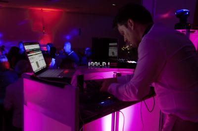 Un DJ mixe sur un ordinateur portable, entouré de lumières colorées dans un décor en bois avec des bouées suspendues.