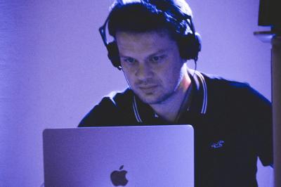 Un DJ mixe sur un ordinateur portable, entouré de lumières colorées dans un décor en bois avec des bouées suspendues.