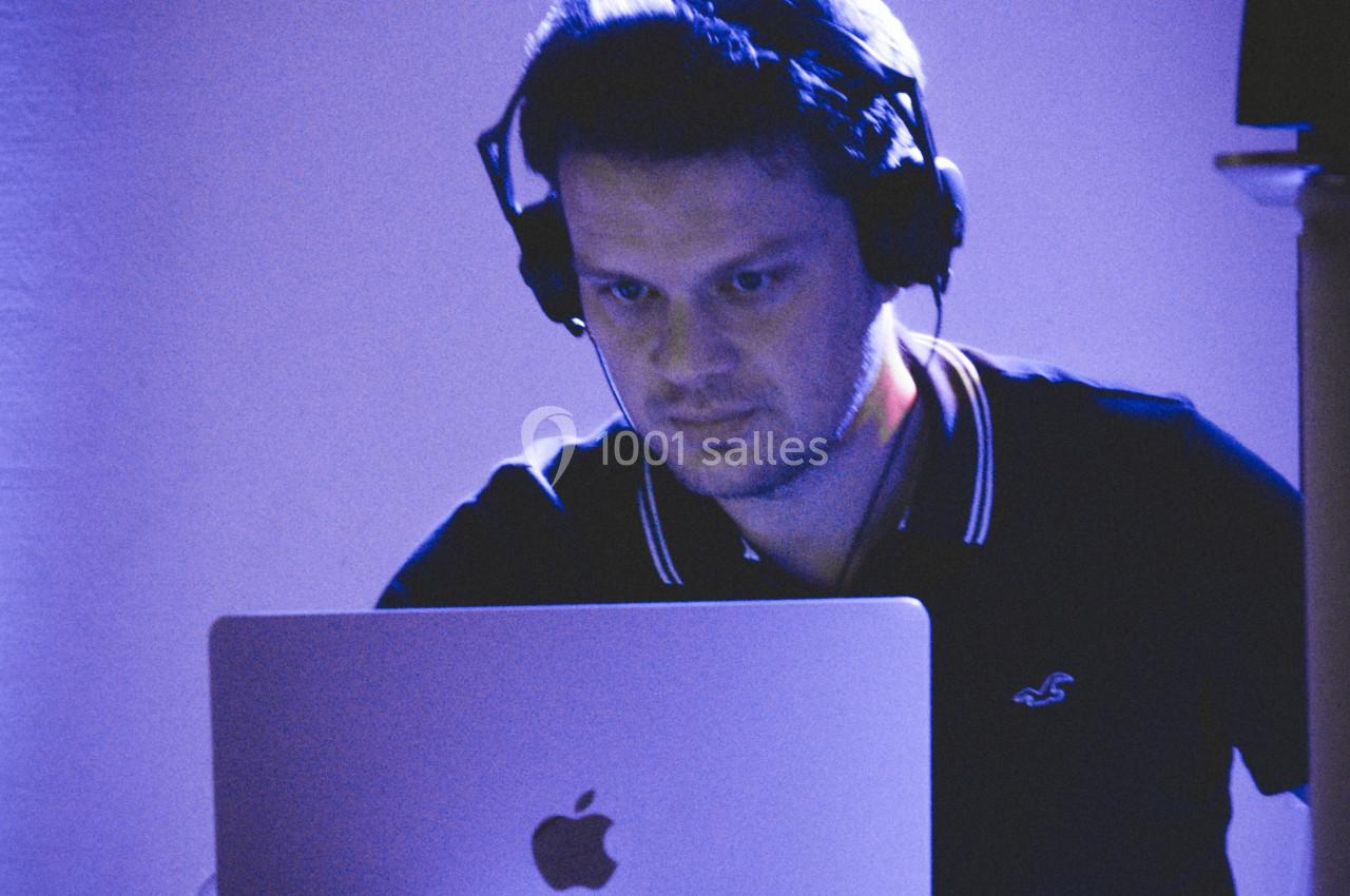 Homme portant un casque audio, concentré sur un ordinateur portable dans une ambiance lumineuse bleutée.