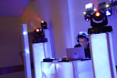Un DJ mixe sur un ordinateur portable, entouré de lumières colorées dans un décor en bois avec des bouées suspendues.