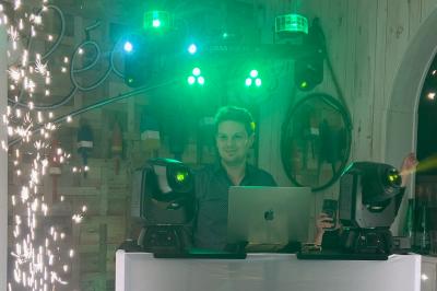 Un DJ mixe sur un ordinateur portable, entouré de lumières colorées dans un décor en bois avec des bouées suspendues.