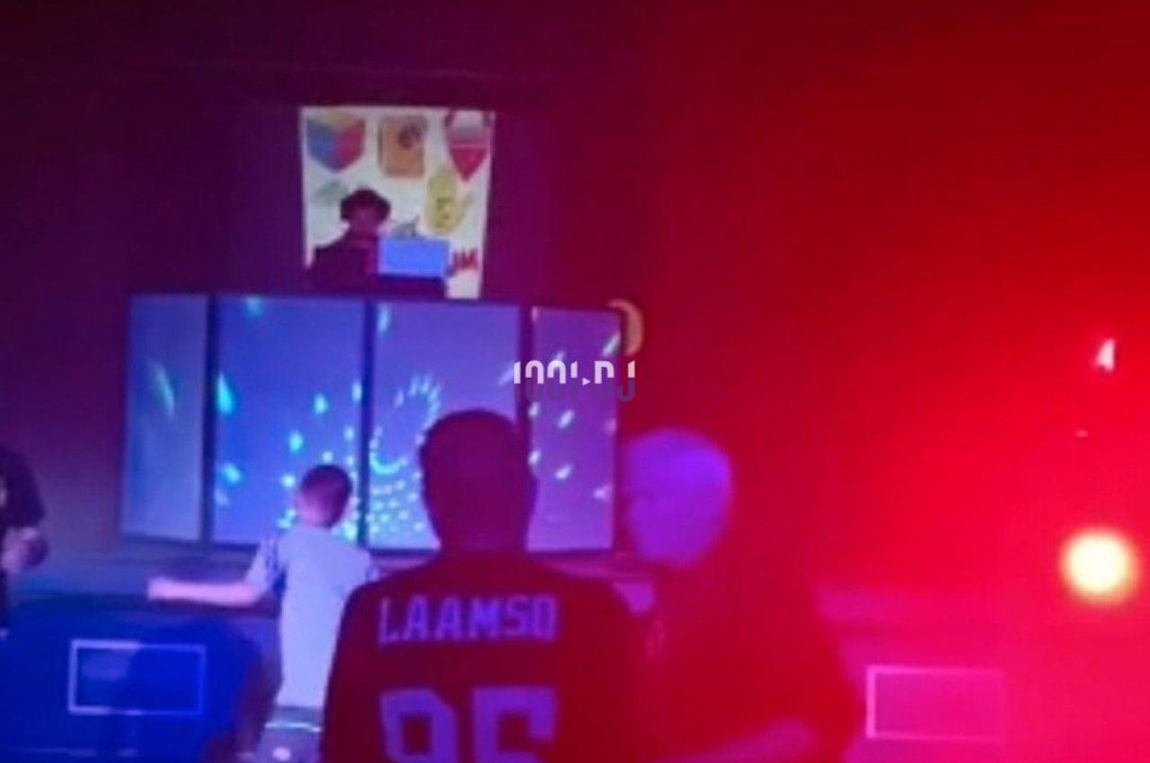 Des personnes dansent dans une salle sombre éclairée par des lumières colorées, avec un DJ en arrière-plan.