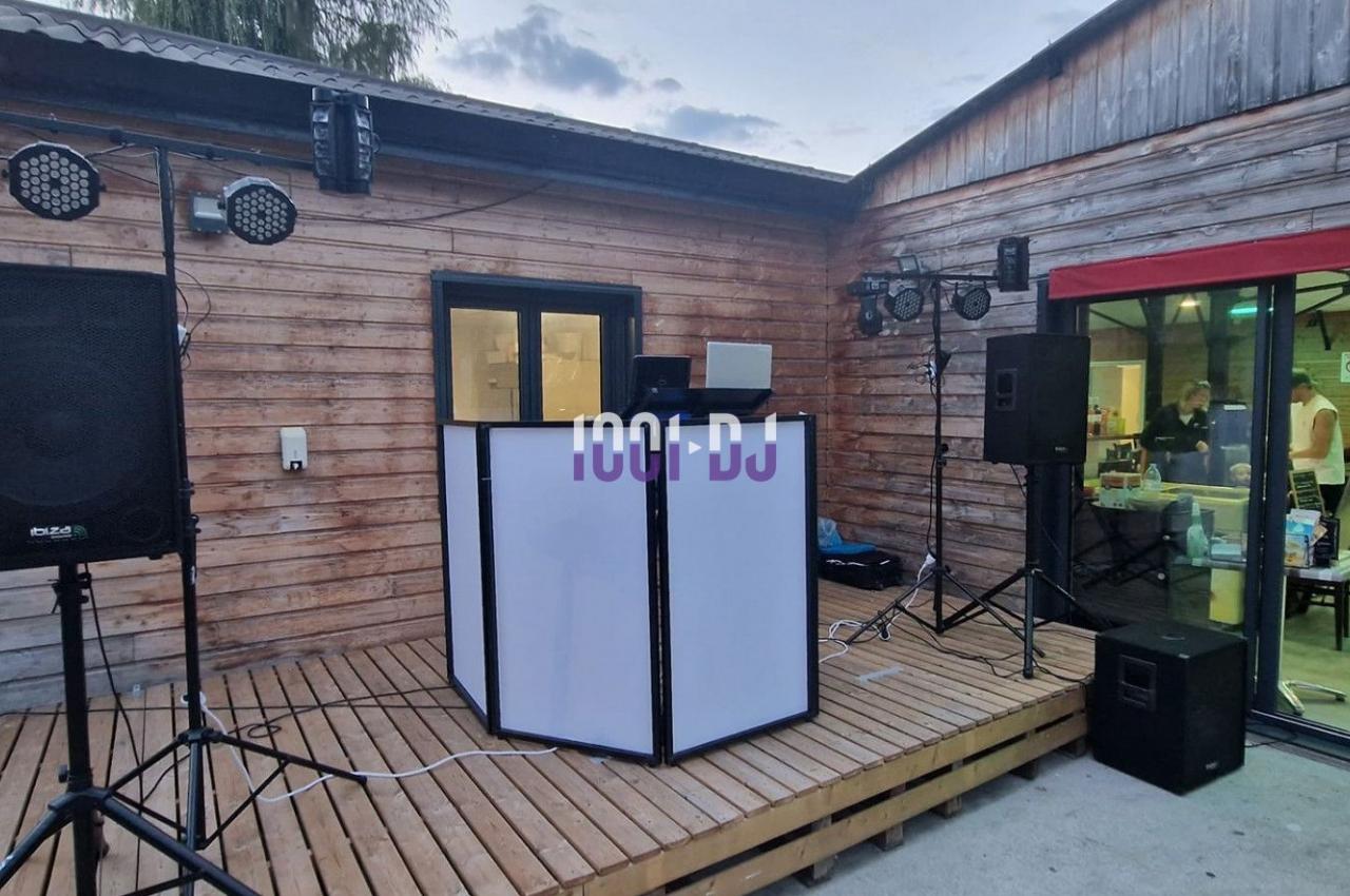 Installation de matériel DJ avec enceintes et éclairages sur une terrasse en bois devant un bâtiment.