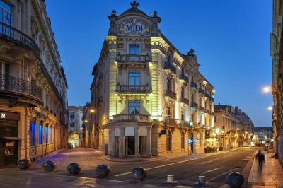 Escalier en marbre avec une rampe en bois, éclairé par des vitraux colorés et des appliques murales sur des murs rouges.