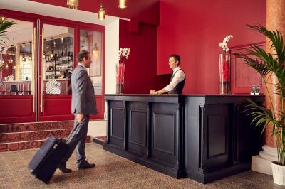 Escalier en marbre avec une rampe en bois, éclairé par des vitraux colorés et des appliques murales sur des murs rouges.