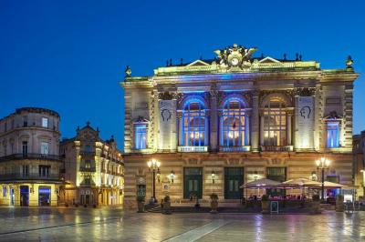 Escalier en marbre avec une rampe en bois, éclairé par des vitraux colorés et des appliques murales sur des murs rouges.
