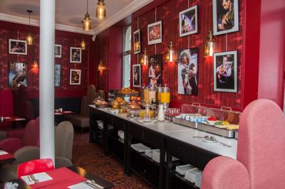 Escalier en marbre avec une rampe en bois, éclairé par des vitraux colorés et des appliques murales sur des murs rouges.