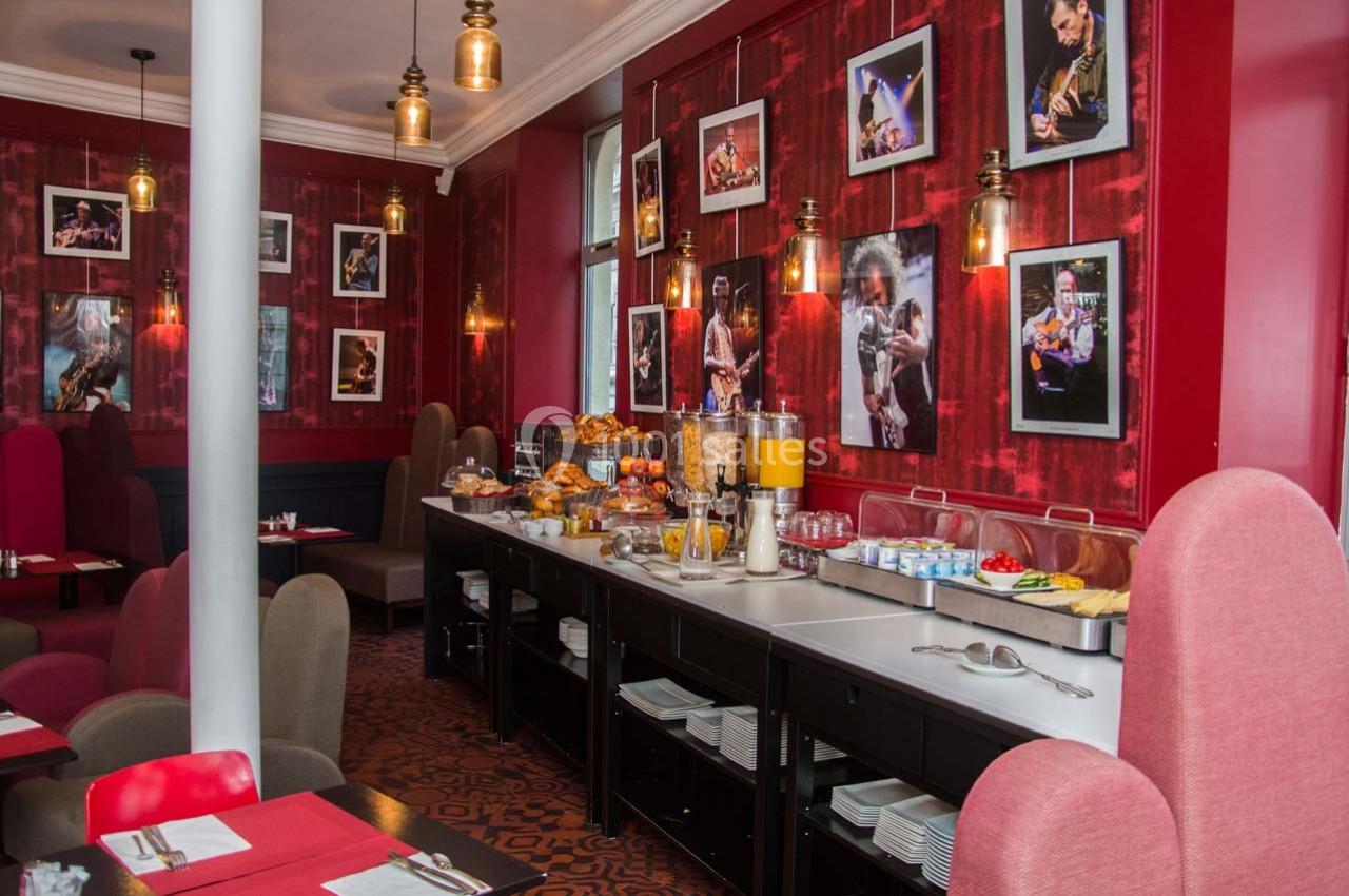 Salle de restaurant avec buffet de petit-déjeuner, décorée de photos encadrées et éclairée par des suspensions lumineuses.