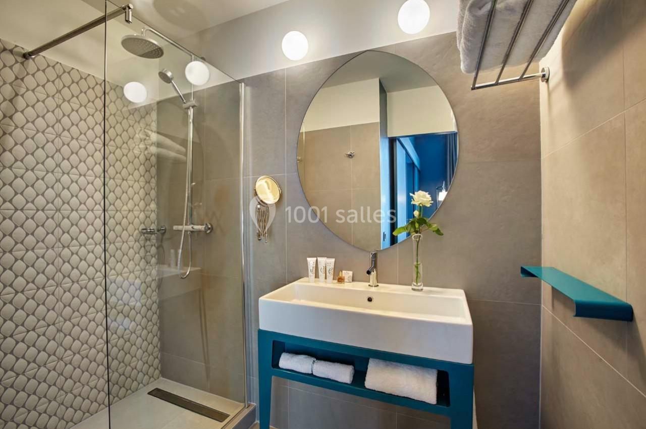 Salle de bain moderne avec douche vitrée, lavabo avec miroir rond, éclairage mural et décoration minimaliste.