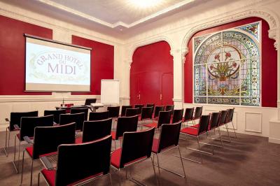 Escalier en marbre avec une rampe en bois, éclairé par des vitraux colorés et des appliques murales sur des murs rouges.