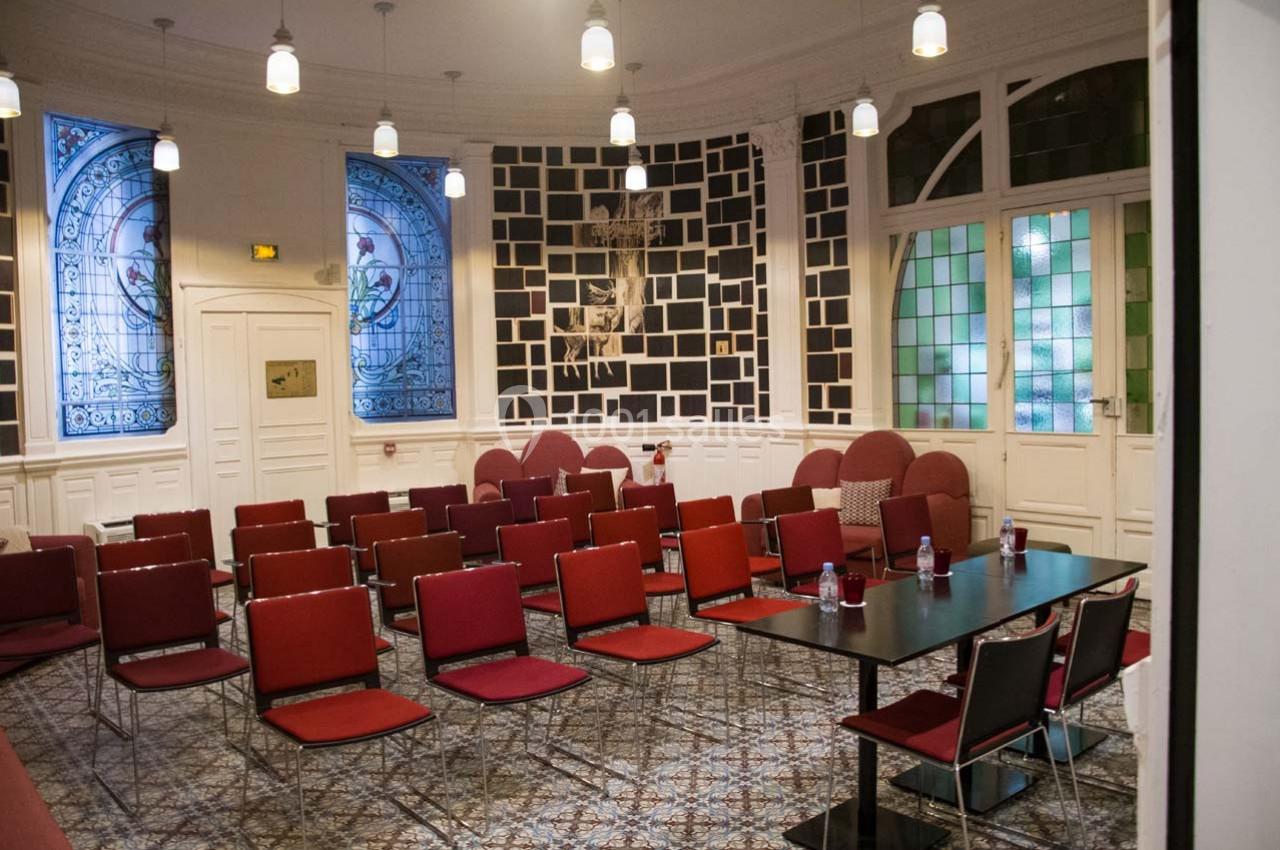 Salle de réunion lumineuse avec des chaises rouges, des vitraux décoratifs et un sol en carrelage.