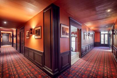 Escalier en marbre avec une rampe en bois, éclairé par des vitraux colorés et des appliques murales sur des murs rouges.