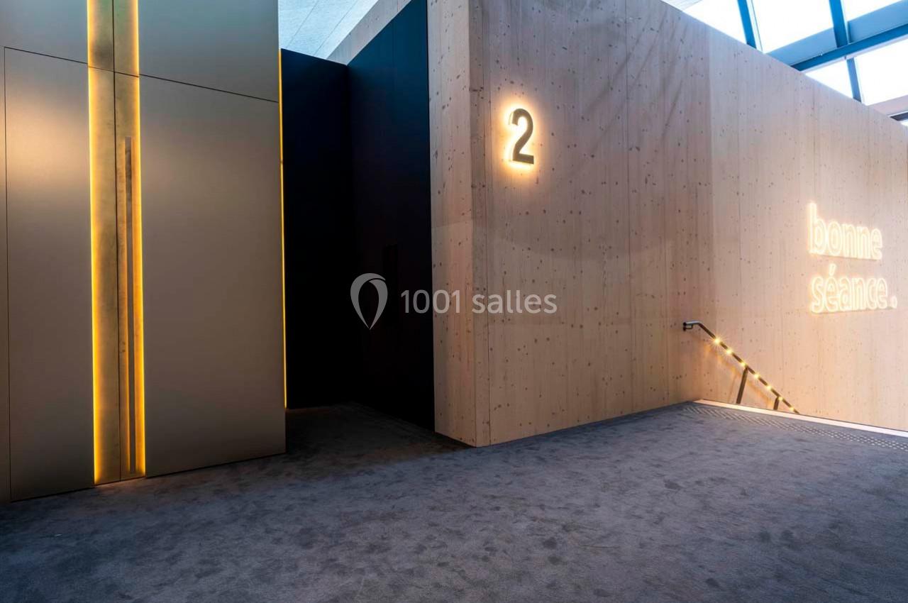 Entrée d'une salle de cinéma avec mur en bois, numéro 2 illuminé et inscription ’bonne séance’ sur le côté.