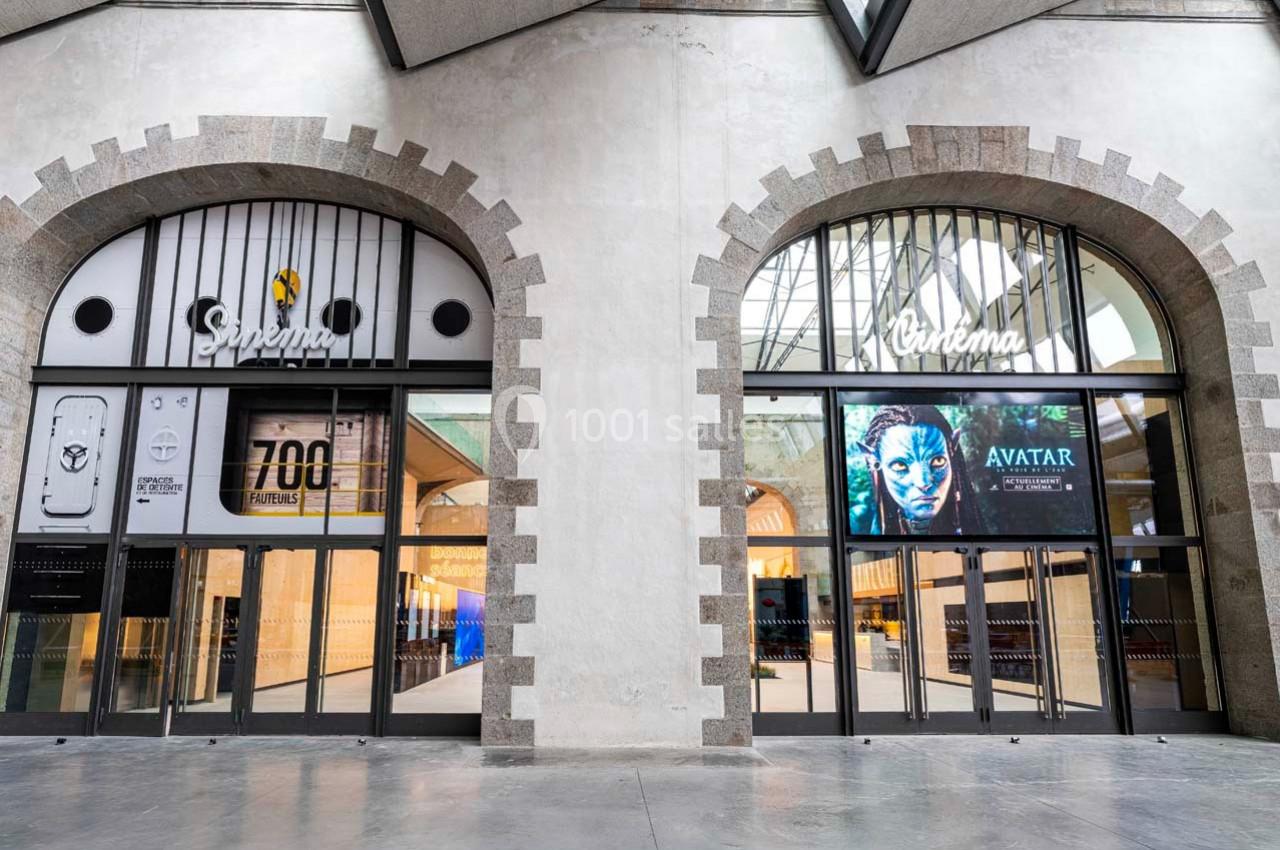 Façade d'un cinéma avec deux grandes portes vitrées, affiches de films et architecture en pierre apparente.