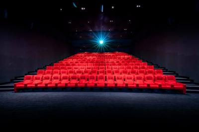 Façade d'un cinéma avec deux grandes portes vitrées, affiches de films et architecture en pierre apparente.
