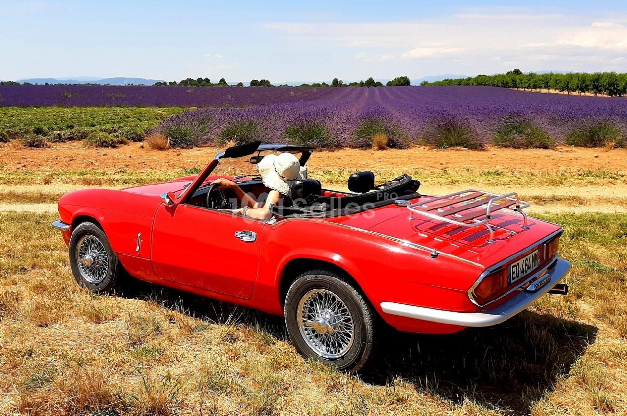 Voiture décapotable rouge garée dans un champ de lavande sous un ciel dégagé.