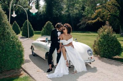 Voiture décapotable classique beige stationnée sur une allée gravillonnée entourée de haies vertes.