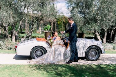 Voiture décapotable classique beige stationnée sur une allée gravillonnée entourée de haies vertes.