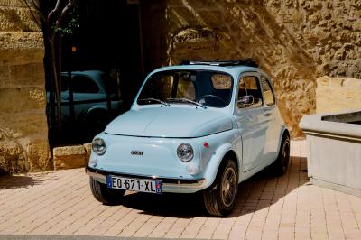 Voiture décapotable classique beige stationnée sur une allée gravillonnée entourée de haies vertes.