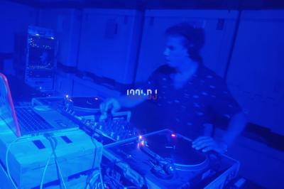 Deux platines vinyles et une table de mixage installées en extérieur sous des parasols, avec des tables en arrière-plan.