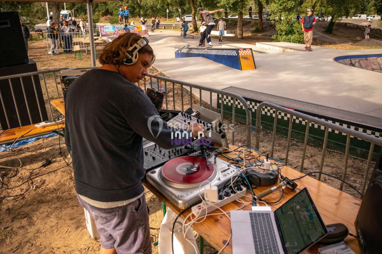 Un DJ mixe sur une platine vinyle lors d'un événement en plein air près d'un skatepark.
