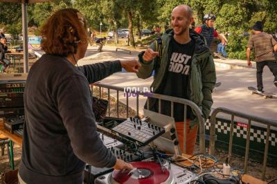 Deux platines vinyles et une table de mixage installées en extérieur sous des parasols, avec des tables en arrière-plan.