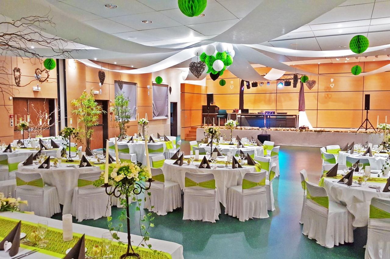 Salle de réception décorée avec des tables dressées, des chaises ornées de rubans verts et des suspensions en papier.