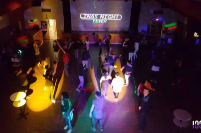 Salle de réception décorée avec des tables rondes, nappes blanches, chaises transparentes et guirlandes lumineuses.