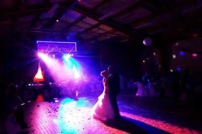 Salle de réception décorée avec des tables rondes, nappes blanches, chaises transparentes et guirlandes lumineuses.