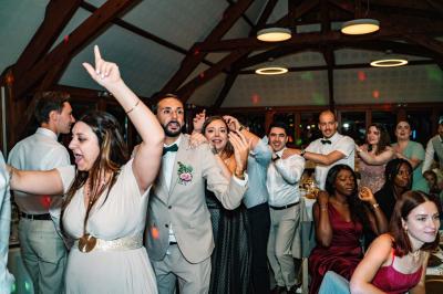Salle de réception décorée avec des tables rondes, nappes blanches, chaises transparentes et guirlandes lumineuses.