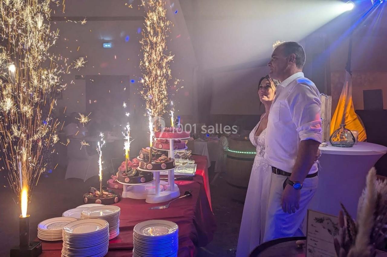 Un couple en tenue de mariage observe une table de desserts illuminée par des fontaines de feu dans une salle festive.