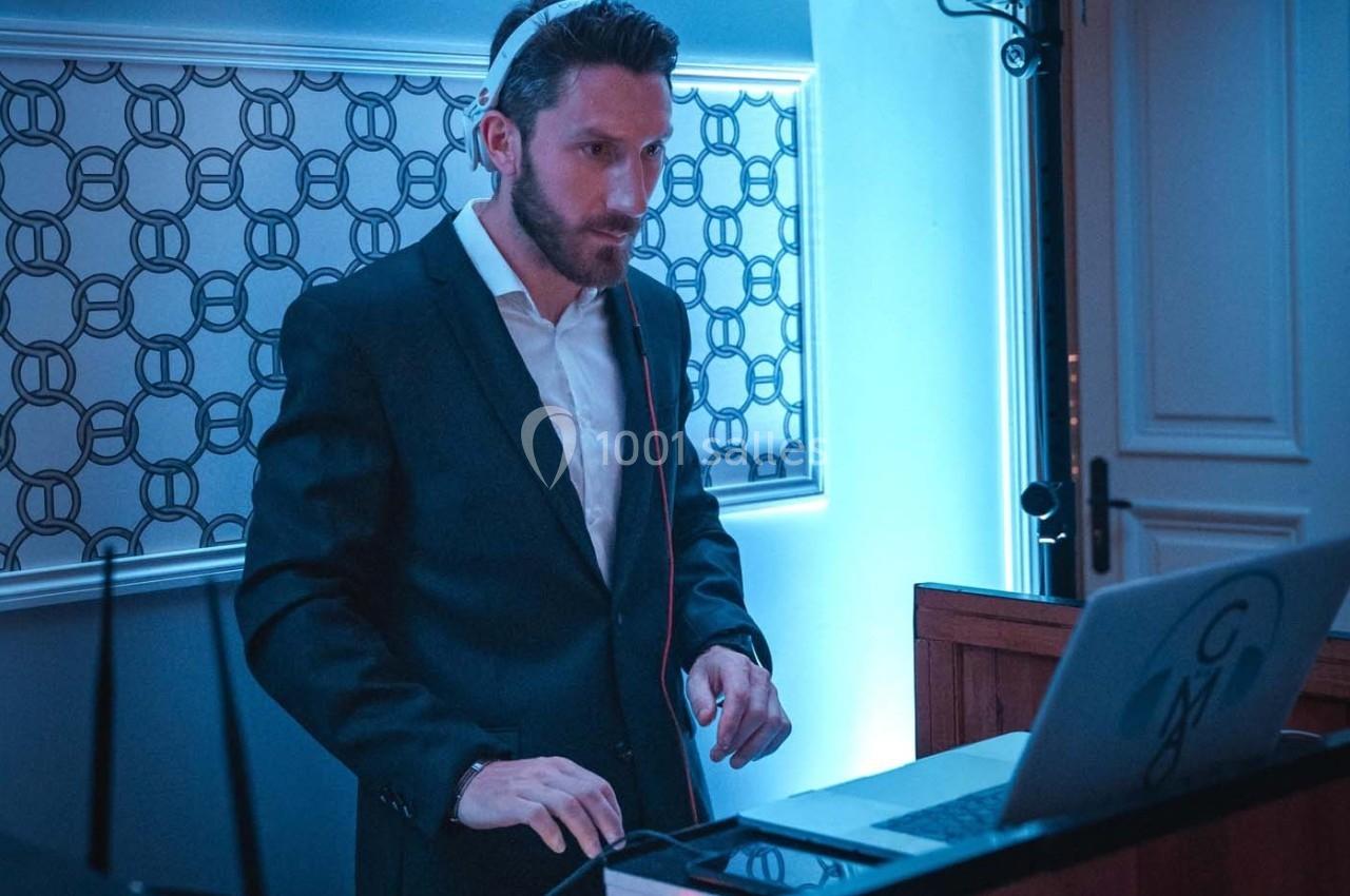 Un DJ en costume mixe de la musique sur un ordinateur portable dans un environnement éclairé en bleu.