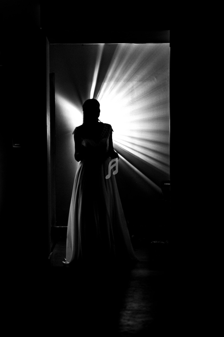 Silhouette d'une femme en robe longue, éclairée par une lumière rayonnante dans un couloir sombre.