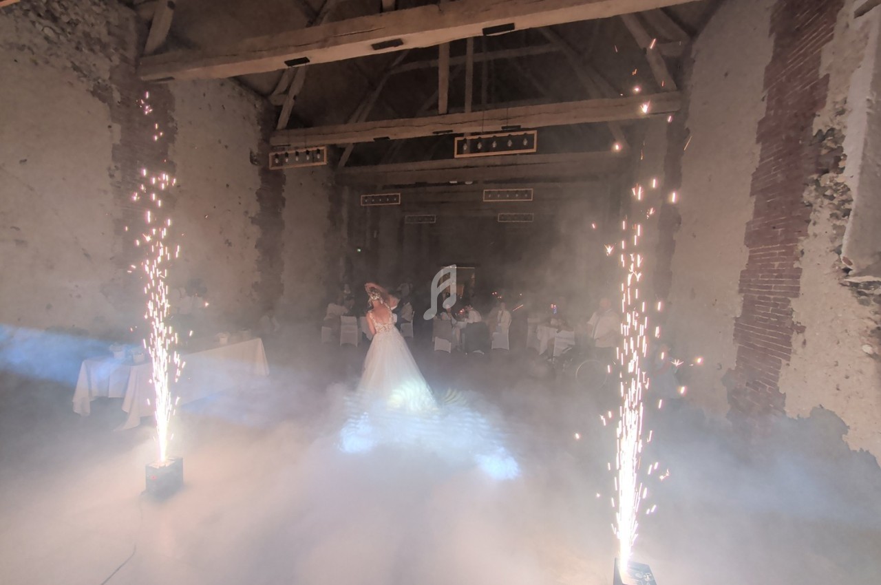 Mariée dans une salle en pierre avec effets de fumée et étincelles, entourée de tables dressées.