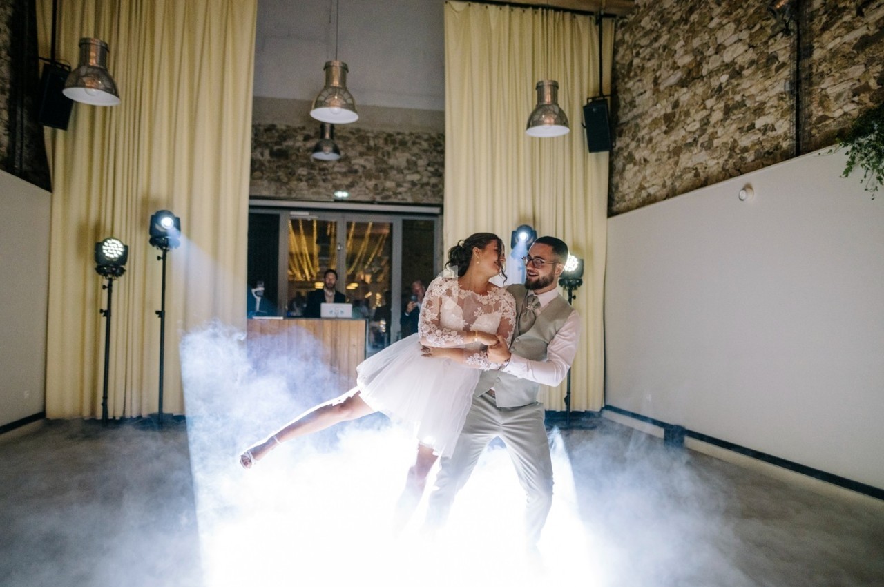 Un couple danse dans une salle éclairée, entouré de fumée et de lumières de scène.