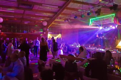 Salle de réception décorée avec des tables rondes, nappes blanches, chaises transparentes et guirlandes lumineuses.