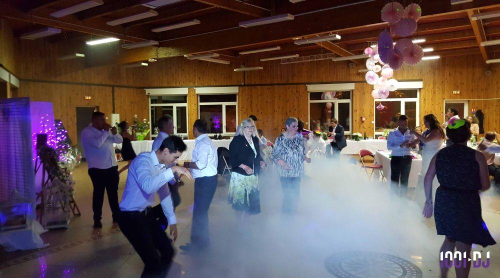 Des personnes dansent sur une piste éclairée, entourées de fumée et de décorations festives dans une salle en bois.