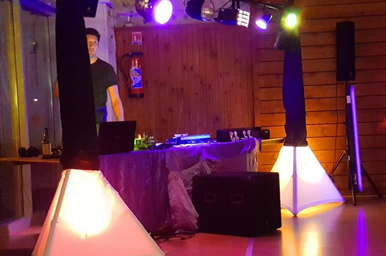 Installation de matériel de son et lumière dans une salle avec un DJ en arrière-plan.