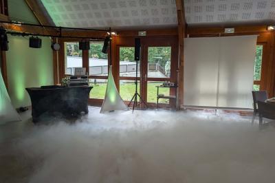 Salle de réception décorée avec des tables rondes, nappes blanches, chaises transparentes et guirlandes lumineuses.