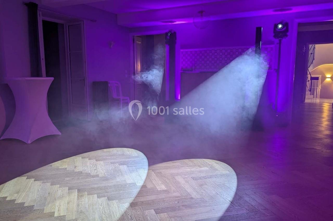 Salle éclairée par des projecteurs violets, avec un sol en parquet et de la fumée diffusée dans l'air.